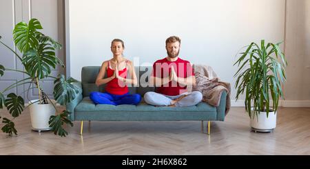 A middle-aged couple is meditating while sitting on the couch. The concept of mental health and a healthy lifestyle. Format photo 2x1. Stock Photo
