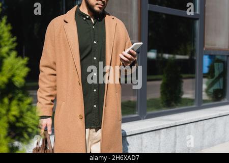 cropped view of man in beige coat using smartphone outdoors Stock Photo