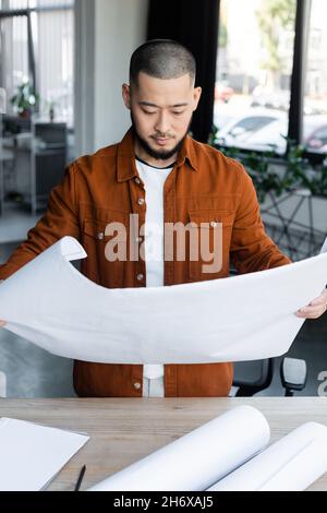 asian engineer looking at blueprint while working in architectural bureau Stock Photo