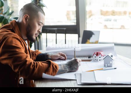 asian architect drawing blueprint while working on architectural project in office Stock Photo
