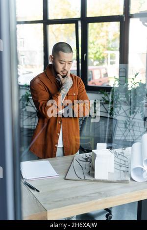 pensive asian architect looking at house models on desk in office on blurred foreground Stock Photo