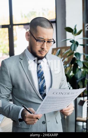 serious asian businessman holding pen while reading contract in office Stock Photo