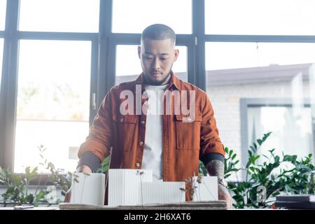 asian architect holding construction project while standing against windows in office Stock Photo