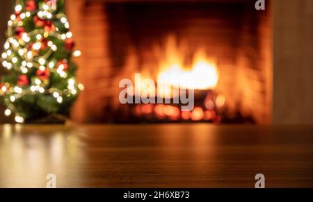 Christmas tree and burning fireplace, blur bonfire fire flames and festive decoration lights. Wooden table empty, space. Advertise template Stock Photo