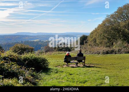 An elderly couple enjoying the sunny autumn day seated on a bench on top of the North Downs at Newlands Corner near Guildford Surrey England UK Stock Photo