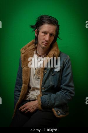 Man with black hair sitting near dark green wall Stock Photo