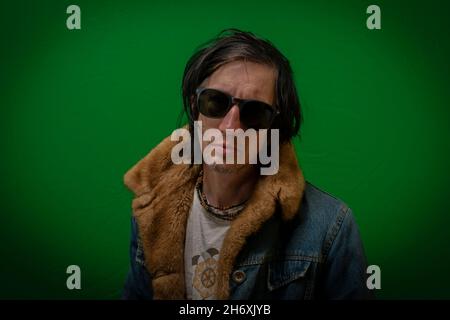 Man with black hair sitting near dark green wall Stock Photo