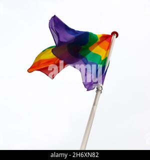 The rainbow flag waves in the wind and is visible on a white background. Stock Photo