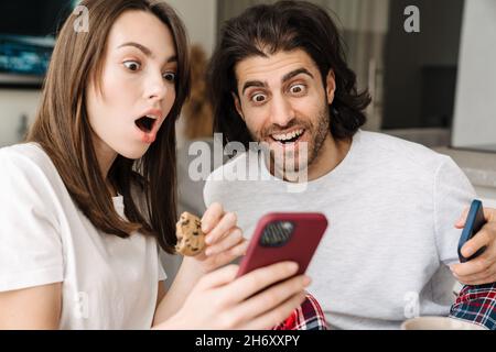 Young multiracial couple using cellphones while having breakfast together at home Stock Photo