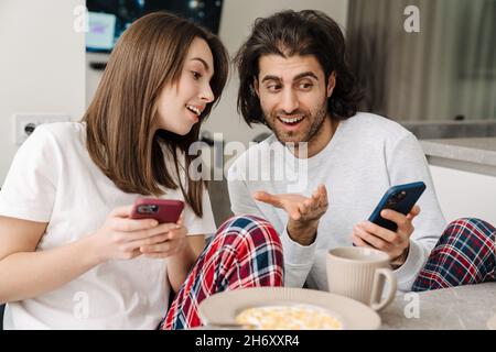 Young multiracial couple using cellphones while having breakfast together at home Stock Photo