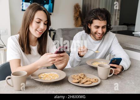 Young multiracial couple using cellphones while having breakfast together at home Stock Photo