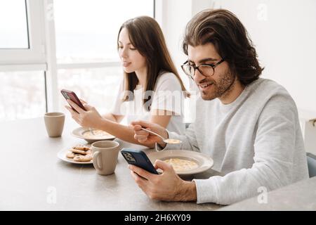 Young multiracial couple using cellphones while having breakfast together at home Stock Photo