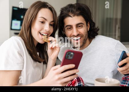 Young multiracial couple using cellphones while having breakfast together at home Stock Photo