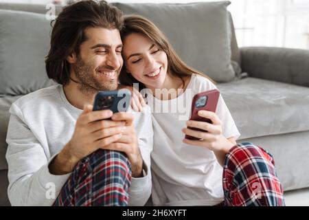 Young multiracial couple using cellphones while sitting together on floor at home Stock Photo