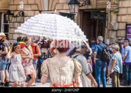 2019 07 25 Bath UK back of woman dressed in Regency Jane Austen period clothing with white ruffled parasol walking among crowd of tourists Stock Photo