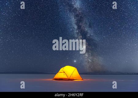 Yellow tent lighted from the inside against the backdrop of incredible starry sky with Milky way. Amazing night landscape. Tourists camp in winter mountains. Travel concept Stock Photo