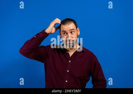Portrait of a confused young man scratching his head isolated over blue background Stock Photo