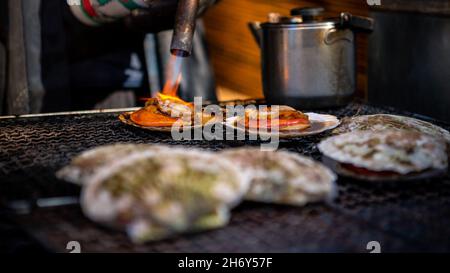 Vendor cooking scallops on steel grill in asian fish market street at Japan. People cooked popular seafood grilling BBQ. Flame fire of charcoal. Famou Stock Photo
