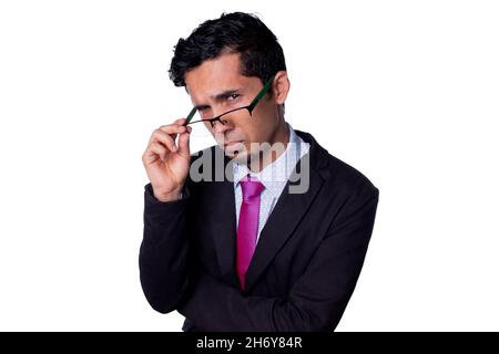 Businessman looking suspiciously at the camera, peering through his glasses with a dubious expression. Young adult latin guy wearing elegant clothes Stock Photo