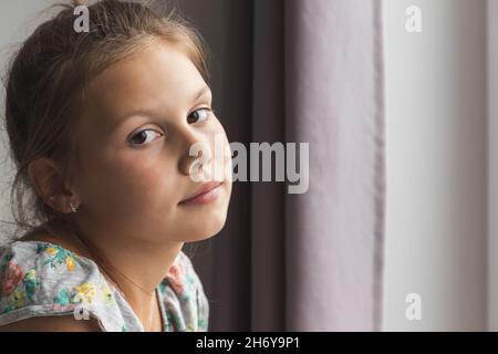 Close up portrait of little Caucasian girl sitting near the window in a room Stock Photo