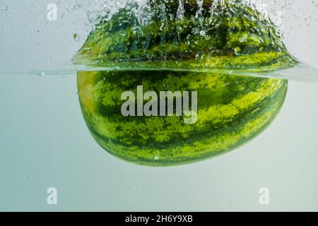 Close up view of watermelon falling into water on turquoise background. Gorgeous backgrounds. Stock Photo