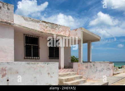 Run down grungy concrete building by the seawall in Mexico with ocean to one side and a beautiful blue cloudy sky overhead Stock Photo