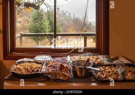 Thanksgiving dinner served in pans on table by window looking outside of cabin in the woods on rainy day Stock Photo