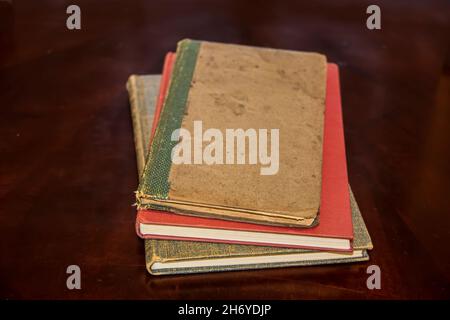 Three old discolored hardback books laying stacked on dark brown surface with foreground - bottoms of books in clear focus and tops blurred out Stock Photo