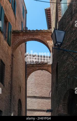 Narrow Street in Historic Center of Siena, Tuscany, Italy. Old brick and stucco houses, arches and cobblestone pavement Stock Photo
