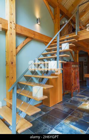Staircase with steel centre spine and pine wood steps leading to upstairs principal bedroom from living room inside timber frame home Stock Photo