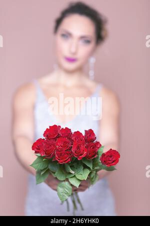 Young woman in a white sleeveless dress presenting a bunch of roses to the camera Stock Photo