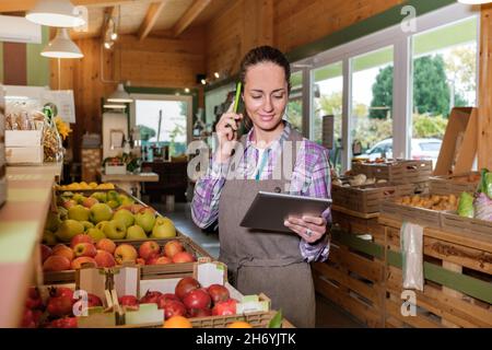 Portrait of happy female sales assistant in a grocery using digital tablet and talking on cell phone while taking inventory Stock Photo