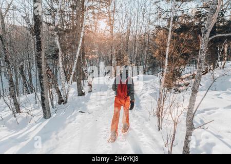 Snowshoeing people in winter forest with snow covered trees on snowy day. Man on hike in snow hiking in snowshoes living healthy active outdoor Stock Photo