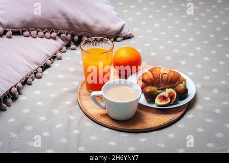 Breakfast in bed. Croissant and figs on a plate, a coffee cup, orange juice and an orange on a tray. Close up. Stock Photo