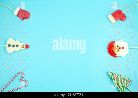Christmas candies in the shape of a snowman, christmas tree, santa claus, mitten on blue background. Lollipops, candy cane. Flat lay, top view. Copy space Stock Photo