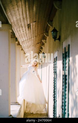 The bride stands on the balcony windowsill holding on to a column in an old house  Stock Photo