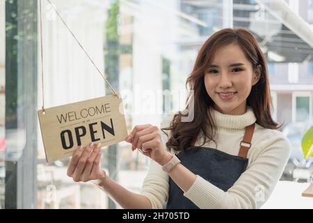 Portrait asian woman smiling and looking to camera in coffee shop. Barista female holding open sign in hand. Working woman small business owner or sme Stock Photo