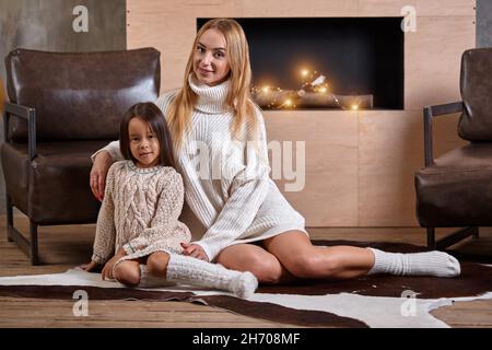 Mom with little girl relaxing on floor near a cozy sofa, Christmas lights in the fireplace Stock Photo