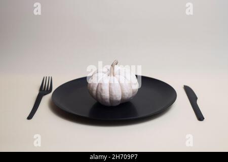 white pumpkin on black plate with black plastic knife and fork isolated on light background. Image contains copy space Stock Photo