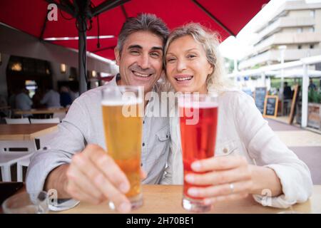 senior couple holding forwards their drinks on restaurant terrace Stock Photo