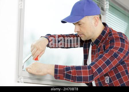 construction worker repairing plastic window with screwdriver indoors Stock Photo