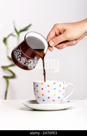 Pouring freshly brewed Turkish black coffee into a cup from a cezve. Stock Photo