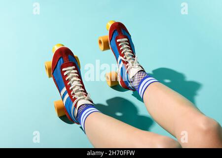 From above of crop anonymous female in bright colorful socks and roller skates resting in sunlight against blue background