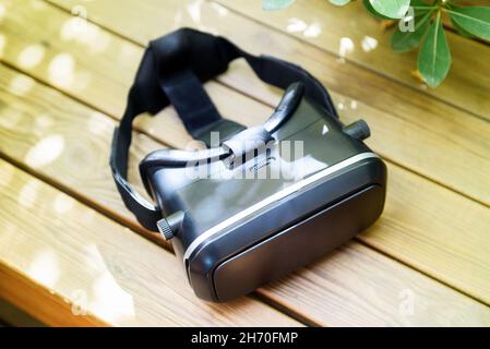 From above of modern black virtual reality glasses placed om wooden table near green potted plant on sunny day Stock Photo