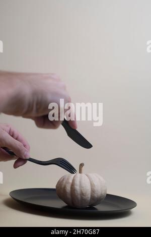person cutting white pumpkin with black plastic knife and fork isolated on light background. Image contains copy space Stock Photo