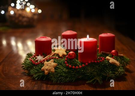 First Advent - decorated Advent wreath from fir branches with red burning candles on a wooden table in the time before Christmas, festive bokeh in the Stock Photo