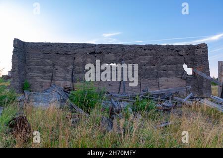 An old gray sullen destroyed wall of a concrete building with rebar outside the city against a blue sky. Close-up Stock Photo