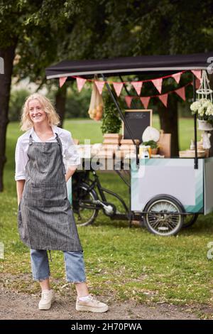 Smiling woman looking at camera, food stall on background Stock Photo