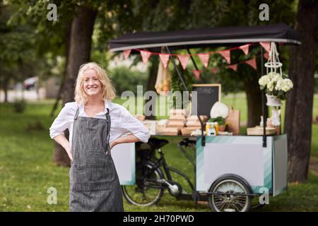 Smiling woman looking at camera, food stall on background Stock Photo
