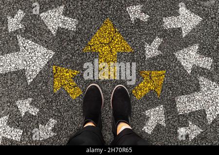Person standing on road with arrow markings pointing in different directions or pathway, decision making concept. Top view. Stock Photo